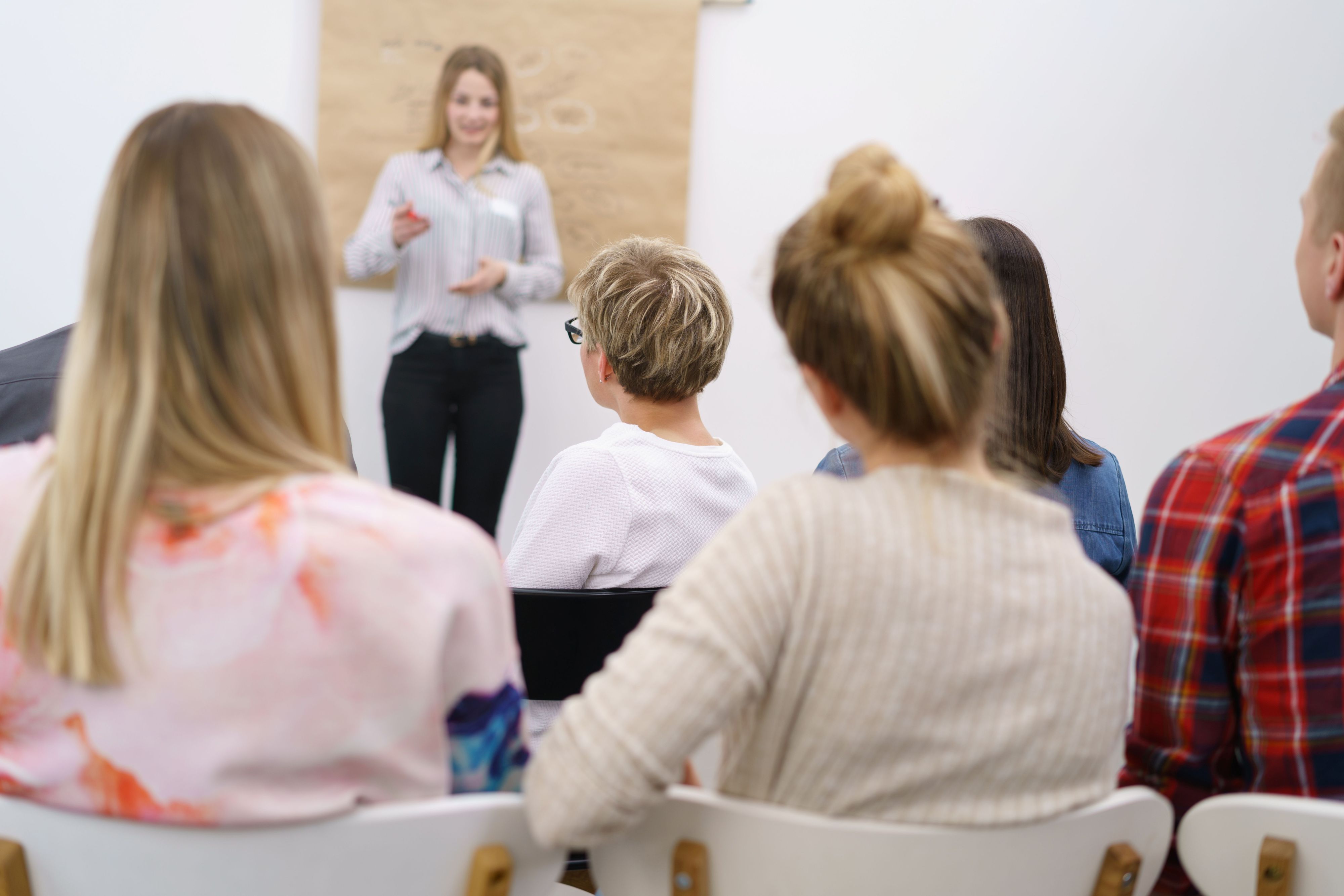 Gruppe von Personen sitzt in einem Schulungsraum und hört einer Vortragenden zu.